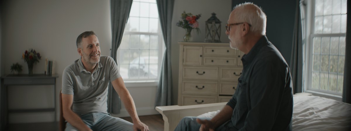 Two adult men having a quiet conversation in a warmly lit room.