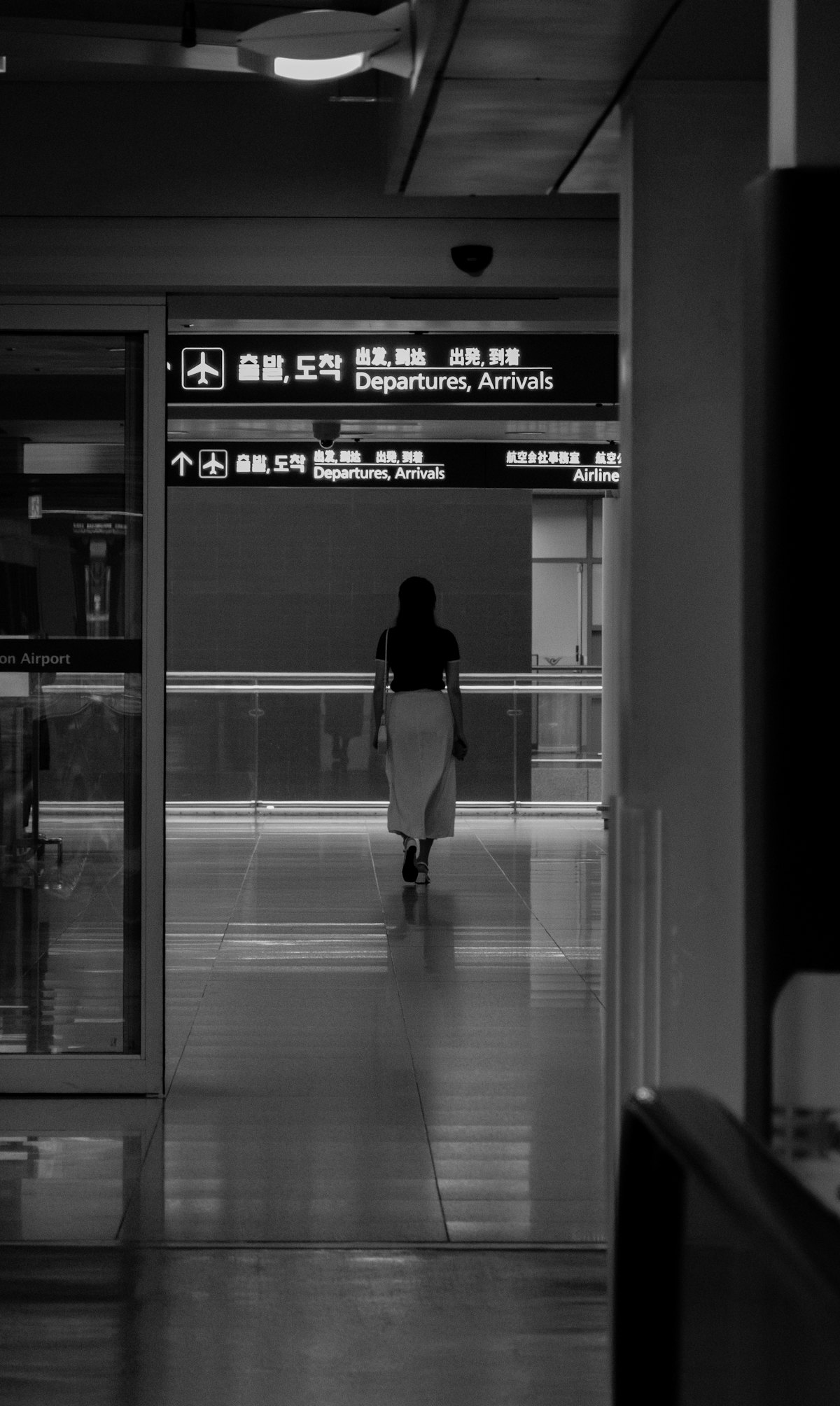 A woman walking alone through an airport terminal with luggage.