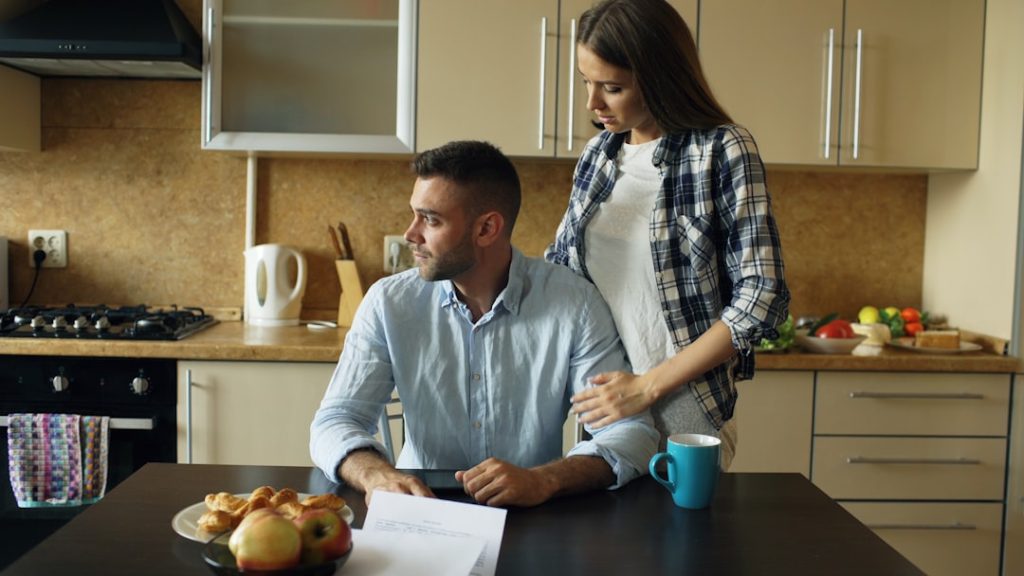 A couple discussing bills at a kitchen table, representing a difficult conversation about family money.