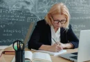 A mature woman studying at a desk in a classroom with a notebook and laptop.
