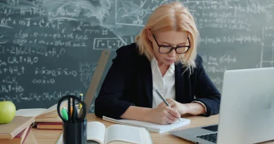 A mature woman studying at a desk in a classroom with a notebook and laptop.
